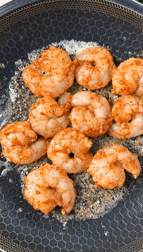 Cajun-seasoned shrimp cooking in bubbling butter in a skillet.