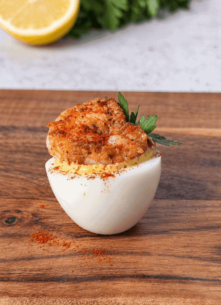 Close-up of an upright Cajun shrimp deviled egg topped with smoked paprika and a fresh herb leaf.