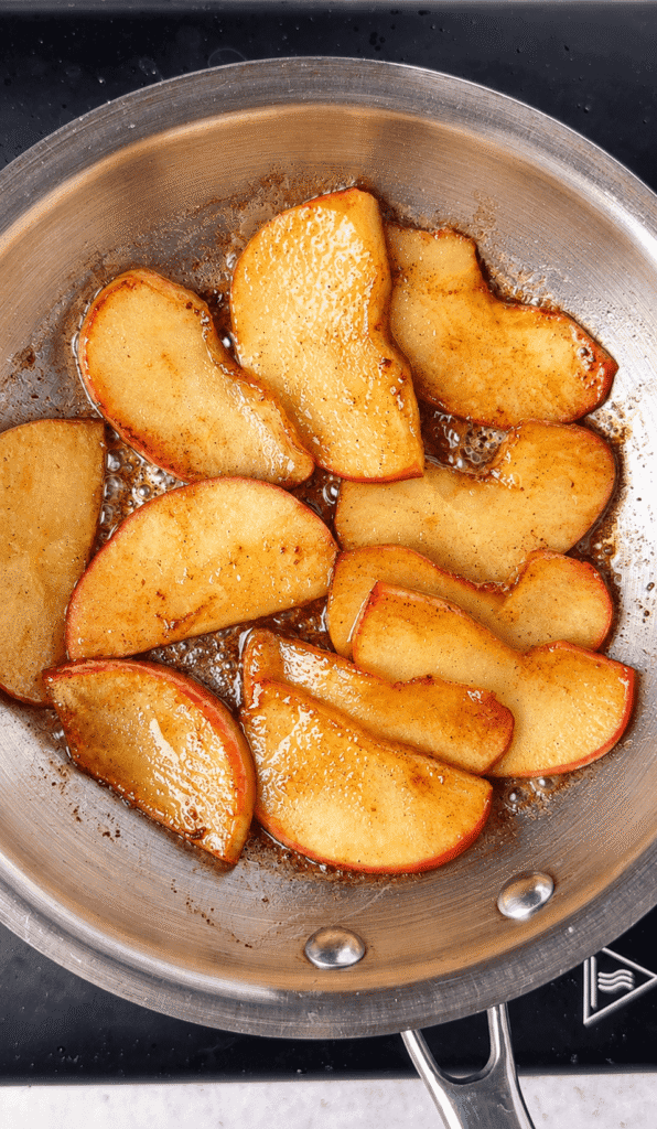 Golden caramelized apple slices with browned edges cooking in a buttery cinnamon glaze.