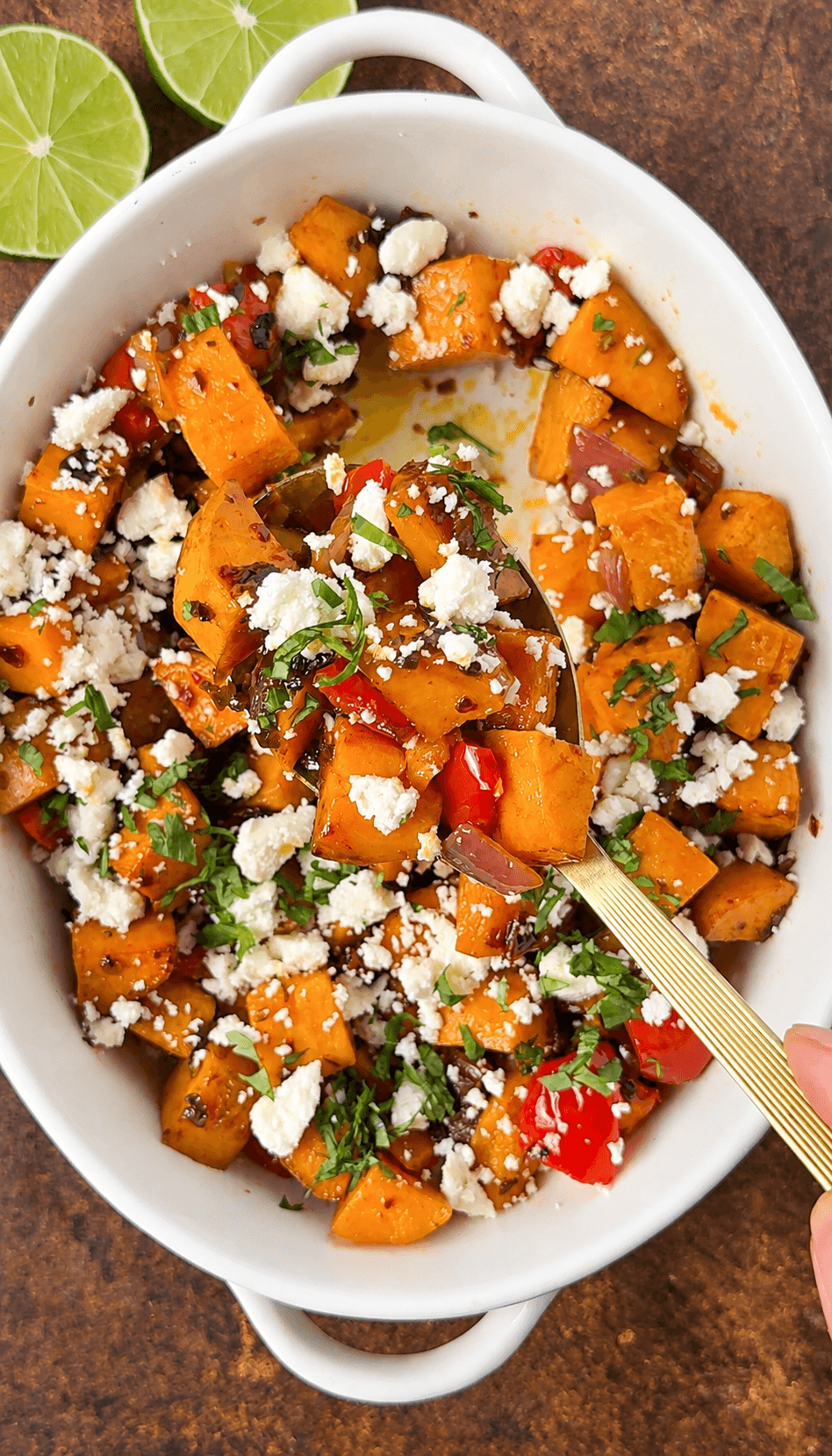 A gold spoon lifting chipotle roasted sweet potatoes, red pepper, and onion topped with cotija and cilantro.