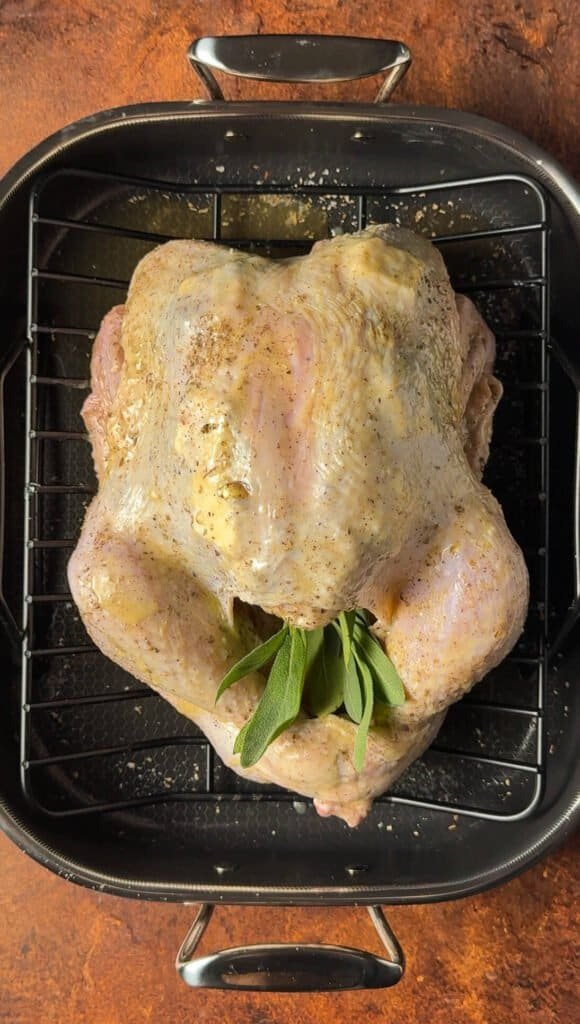 Whole turkey brushed with butter and seasoned with sage, with fresh sage sprigs in the cavity, ready for roasting.