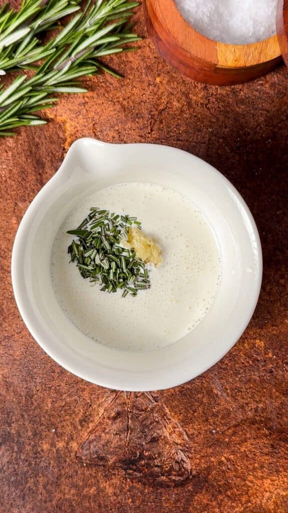 Heavy cream with chopped fresh rosemary and grated garlic in a white bowl