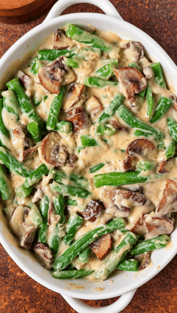 Green beans coated in creamy mushroom sauce in a white oval baking dish before adding the breadcrumb topping.