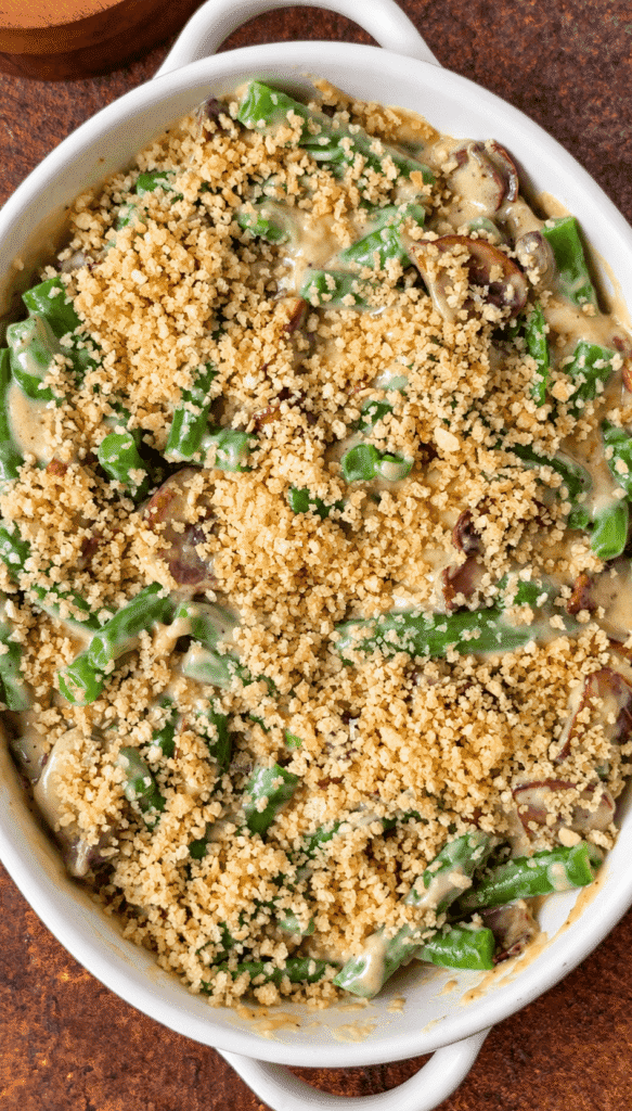 Unbaked green bean casserole with mushrooms and an even layer of panko breadcrumbs in a white baking dish.