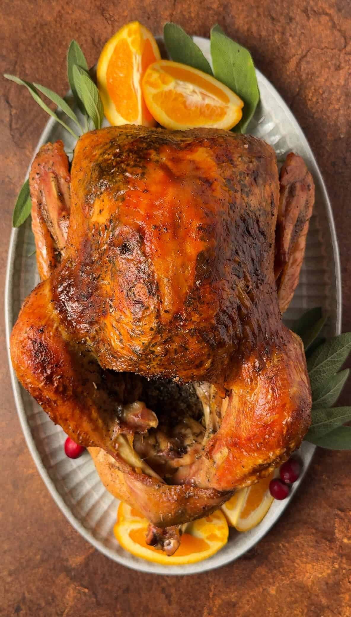 Whole roasted citrus turkey with golden brown skin, garnished with fresh orange wedges, sage leaves, and cranberries on a serving platter.