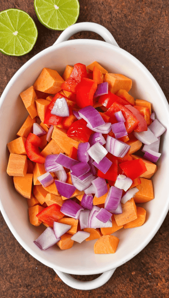 Cubed raw sweet potatoes, red onion, and red bell pepper in a white baking dish.